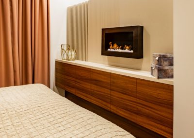 Tmavohnedý nábytok v spálni s krbom na béžovej stene